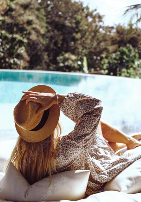 Woman sitting by pool with sunhat